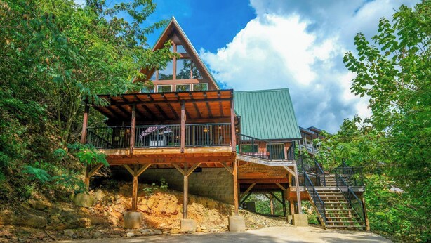 A modern house with a wooden deck, a green roof, and a staircase leading to a second level. - Patriots Den - Comfy Interiors, Cozy fireside nights, Wi-Fi and Porch Swings (Gatlinburg)