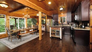 A spacious kitchen with wooden beams, a dining area with a bench, and large windows overlooking greenery. - Patriots Den - Comfy Interiors, Cozy fireside nights, Wi-Fi and Porch Swings (Gatlinburg)