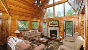 A cozy log cabin interior with a fireplace, comfortable seating, and large windows. - Patriots Den - Comfy Interiors, Cozy fireside nights, Wi-Fi and Porch Swings (Gatlinburg)