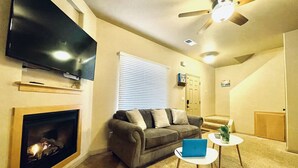 Un salon avec une cheminée, un canapé, un téléviseur et un ventilateur de plafond.