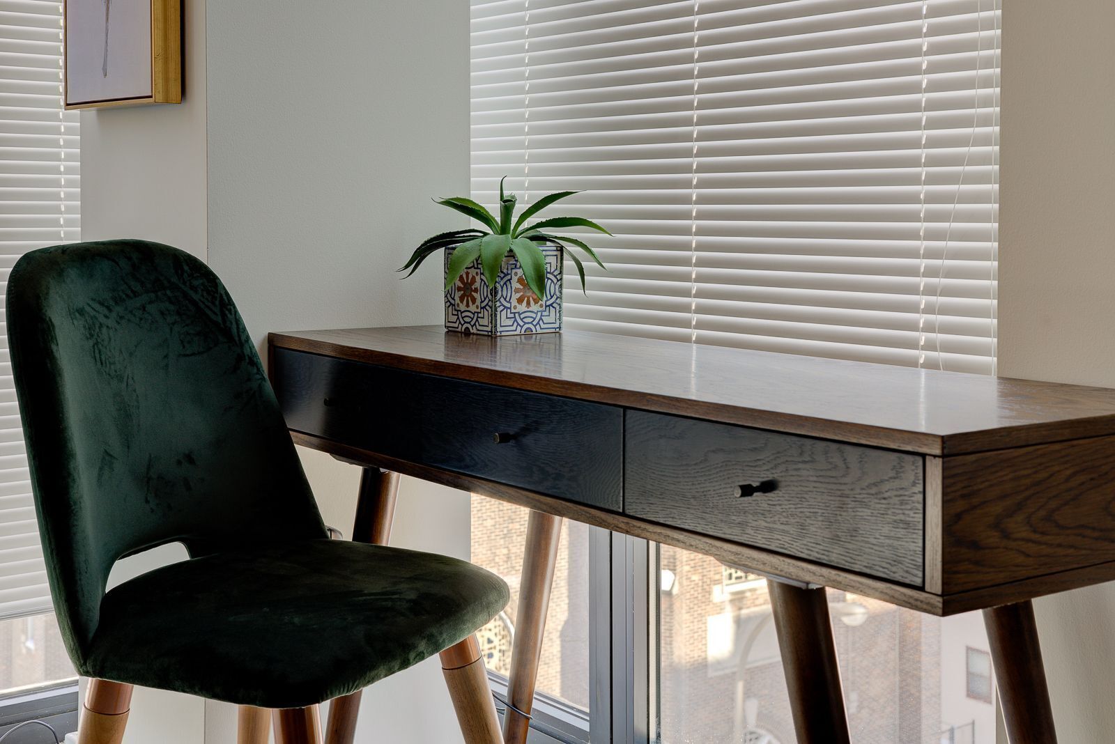 A desk with a drawer, a green chair, and a potted plant on the desk.