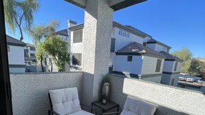 A balcony with two white cushioned chairs, a small table, and a vase with flowers. - 2 Bd/2Ba in Central Phx with a private patio, 2 pools, 2 hot tubs gated complex! (Phoenix)