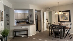 A compact kitchen with a central island, a dining area with a table and chairs, and a living space with a sofa and a TV. - 2 Bd/2Ba in Central Phx with a private patio, 2 pools, 2 hot tubs gated complex! (Phoenix)