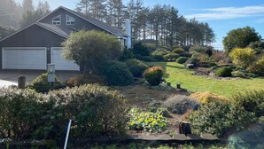 Een woonhuis met garage, een verzorgde tuin en een achtergrond van hoge bomen.