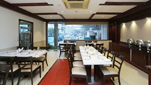 Um restaurante com uma longa mesa de jantar, várias cadeiras e vista para a rua.