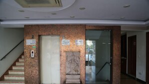 Um hall de hotel com escadaria de mármore, balcão de recepção e porta de vidro que dá para outra área.