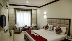 Quarto de hotel com uma cama grande, uma escrivaninha, uma cadeira e uma televisão.