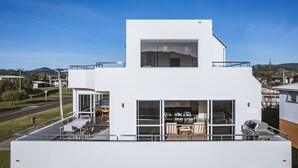 Een modern gebouw met twee verdiepingen, een plat dak, grote ramen en een balkon met buitenmeubilair.