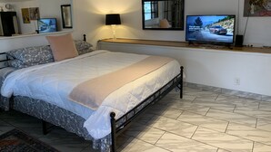 A bedroom with a bed, a TV, a lamp, and a mirror.