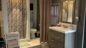 A bathroom with a shower, toilet, and sink. There is a towel rack with towels, a rug, and a mirror on the wall.