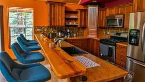 Una cocina con armarios de madera, un refrigerador de acero inoxidable, un microondas y una barra con sillas azules.