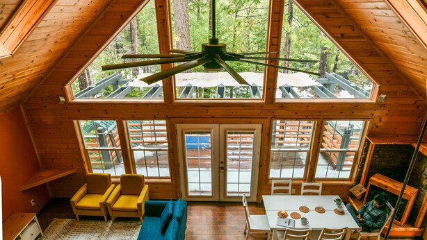 Amplio espacio tipo loft con techo alto, vigas de madera y ventanas grandes que ofrecen vistas del bosque circundante.