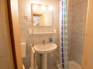 A bathroom with a pedestal sink, a mirror, a shower curtain, and a toilet.