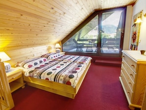 A bedroom with a sloped ceiling, a bed with a patterned duvet, a nightstand, a dresser, and a window with blinds.