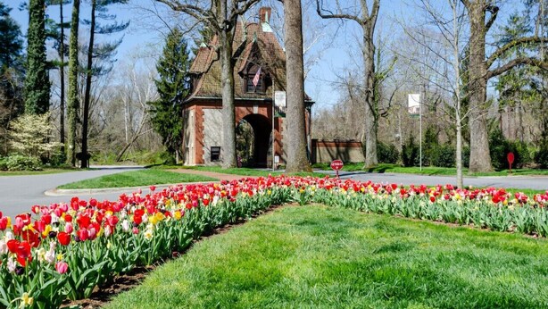 Edificio histórico con un arco de ladrillo, rodeado de un jardín bien cuidado con diversas tulipanes.