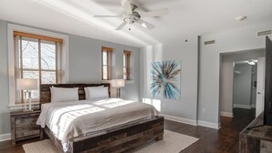 Un dormitorio con una cama de madera, un ventilador de techo y un cuadro abstracto grande en la pared.