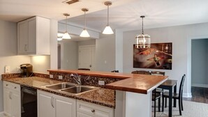 Una cocina moderna con encimeras de granito, armarios blancos e iluminación colgante.