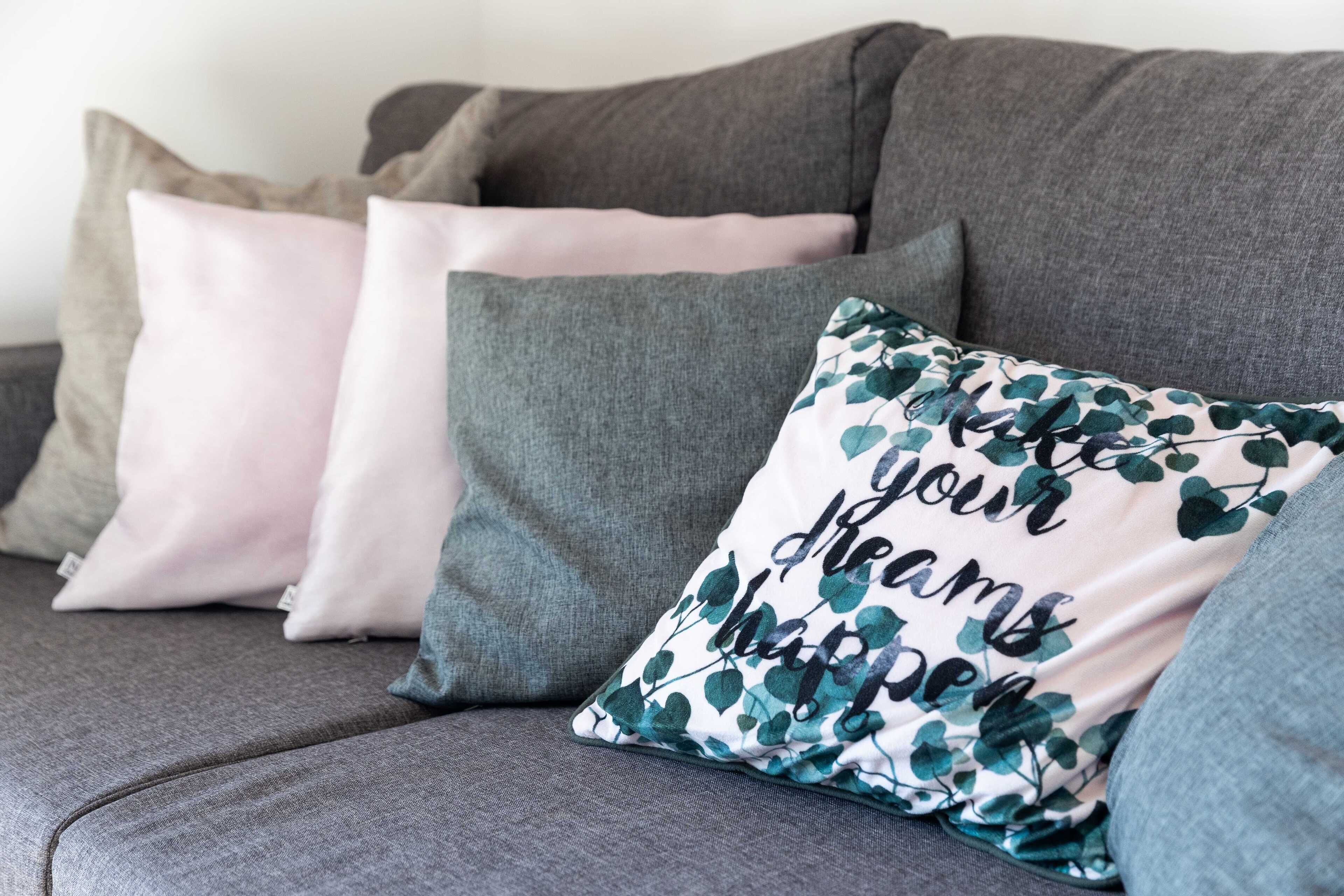 Un canapé gris agrémenté de plusieurs coussins, dont un coussin décoratif orné d’un motif de feuilles et d’un texte.