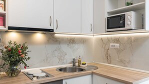 A kitchen with white cabinets, a marble backsplash, a stainless steel sink, a microwave, and a vase with flowers on the counter. - Apartment M&K (Mlini)