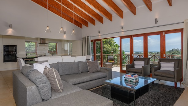 A modern living room with a grey sectional sofa, a coffee table with books, and a view of the outdoors through large windows. - San Lameer Villa Rentals 1603 (Southbroom)