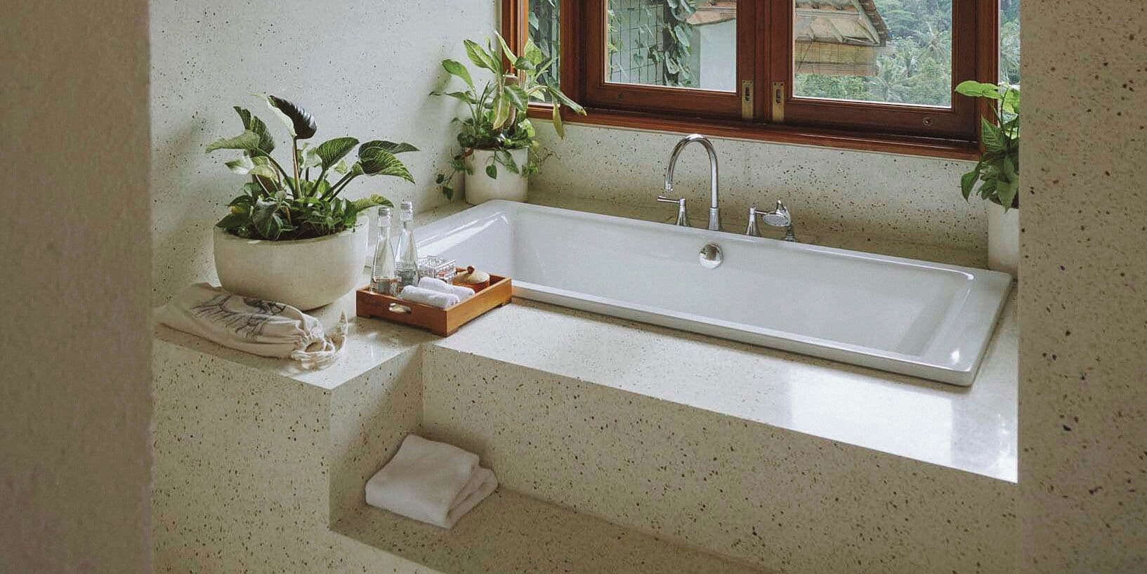 A bathroom with a freestanding bathtub, potted plants, a towel rack, and a window with a view of greenery.