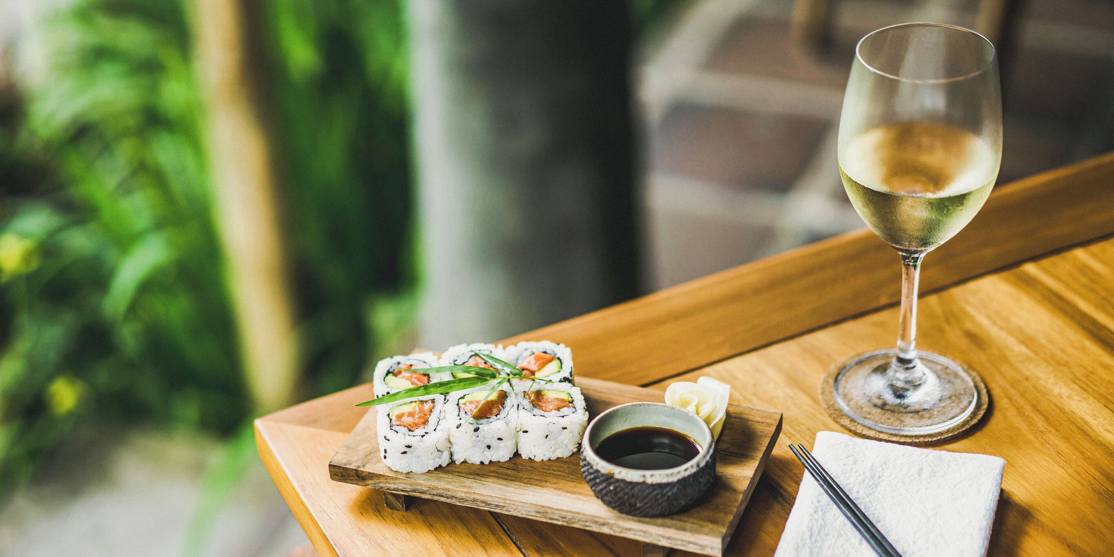 Sushi auf einer Holzschale mit einem Glas Weißwein und Sojasoße auf einem Tisch.