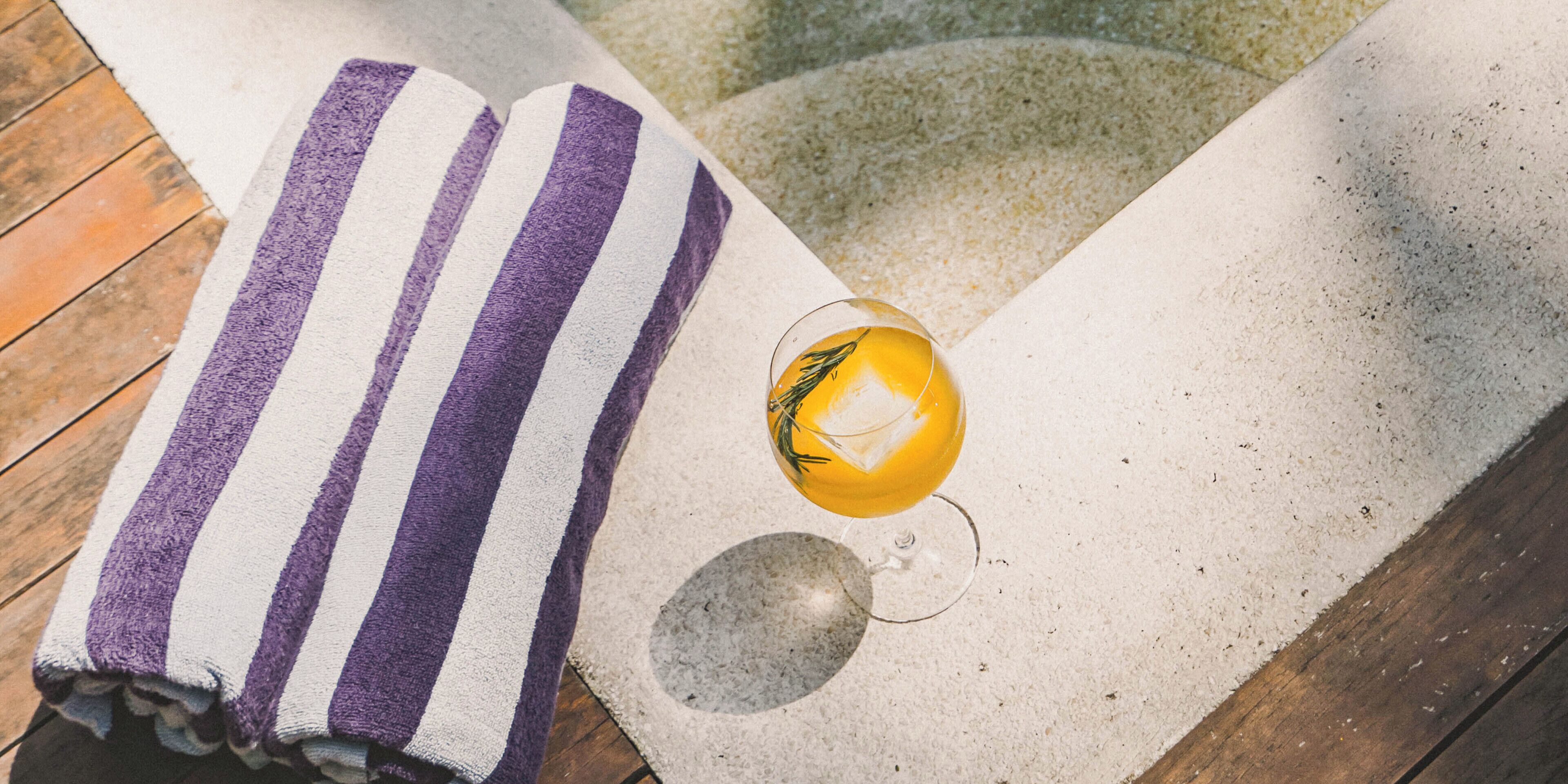 A striped towel and a glass with a yellow drink on a textured surface.