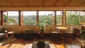 A room with large windows, a sofa, a small table, and a chair. - The Sayan House (Ubud)