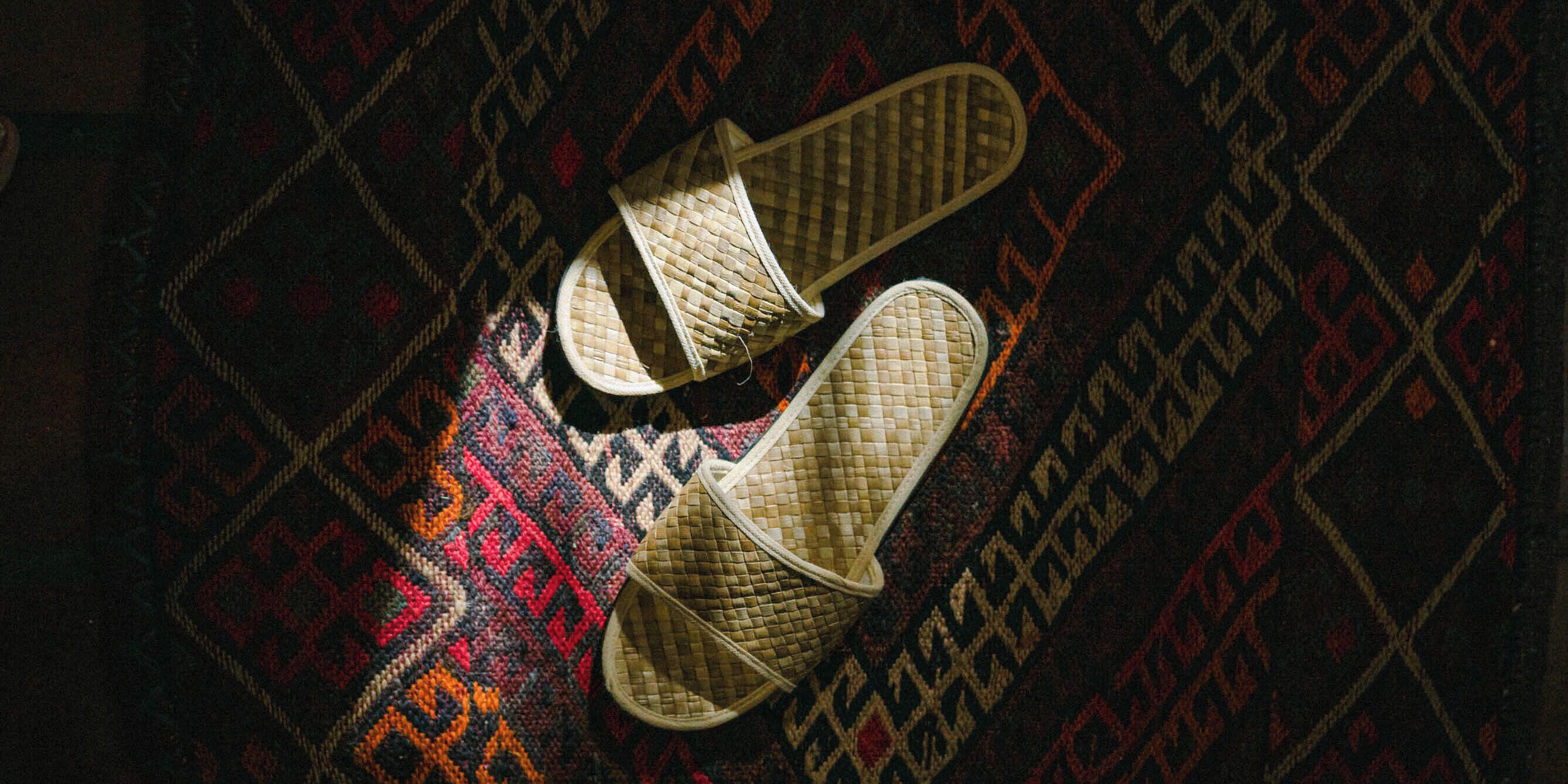 A pair of woven slippers on a patterned carpet.