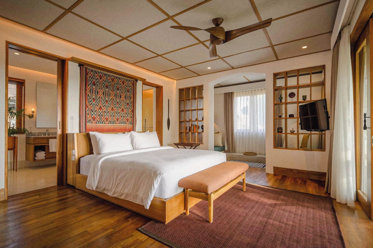 A spacious bedroom with a large bed, a wooden bench, a ceiling fan, and a television.