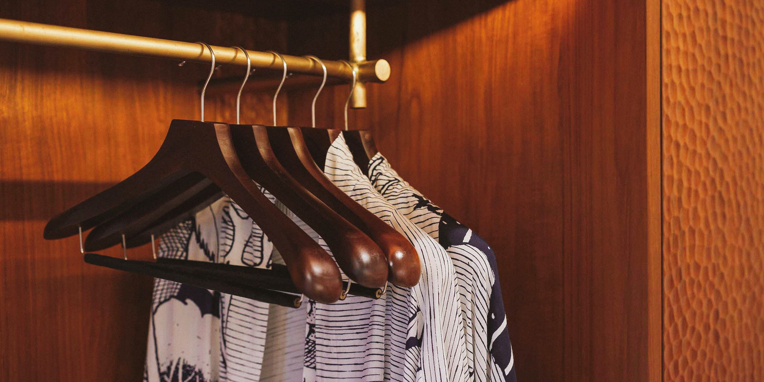 A wooden closet with a hanging rod holding several striped shirts.