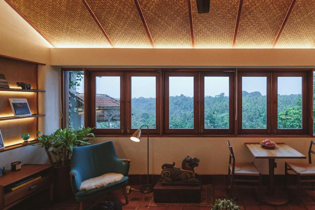 A cozy room with a large window, a desk, a chair, a table, and a small kitchen area.