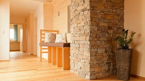 Una habitación con suelo de madera, pared de piedra, una silla de madera con cojín y una planta en maceta.