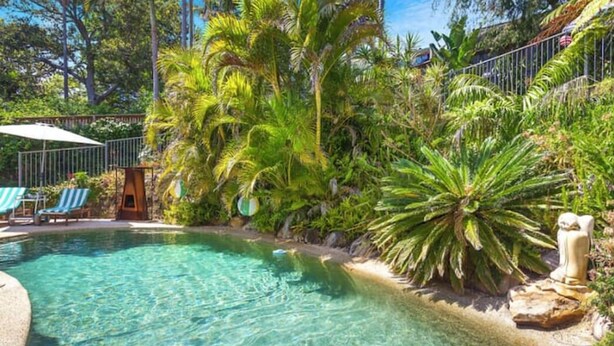 Ein klares Schwimmbecken, umgeben von üppiger tropischer Vegetation und einem Steinweg.