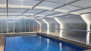Una piscina interior con agua azul cristalina, rodeada de paredes de vidrio y una estructura de techo metálico.