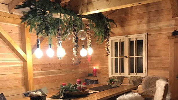 Interno accogliente di una baita di legno con un lungo tavolo da pranzo, sedie e una lampada a sospensione.