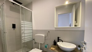 A modern bathroom with a glass-enclosed shower, a white toilet, and a vanity with a large mirror. - Economy Double Room Standard Rate (Cefalù)