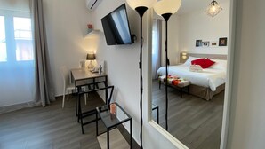 A modern hotel room with a bed, bedside table, chair, TV, and a large mirror. - Economy Double Room Standard Rate (Cefalù)