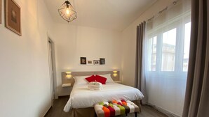 A modern hotel room with a large bed, a bedside table, a wall-mounted light fixture, a window with curtains, and a wooden floor. - Economy Double Room Standard Rate (Cefalù)