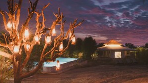 A rustic building with a thatched roof, surrounded by bare trees and a pool. - Brij Pola, Jawai - Luxury Jungle Camp with Private Pools (Bali)