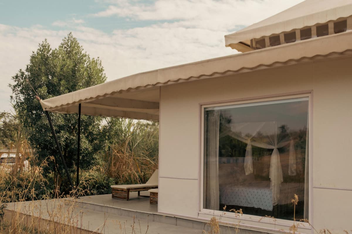Ein modernes Haus mit großem Fenster, einer überdachten Terrasse und Blick auf Bäume und Himmel.