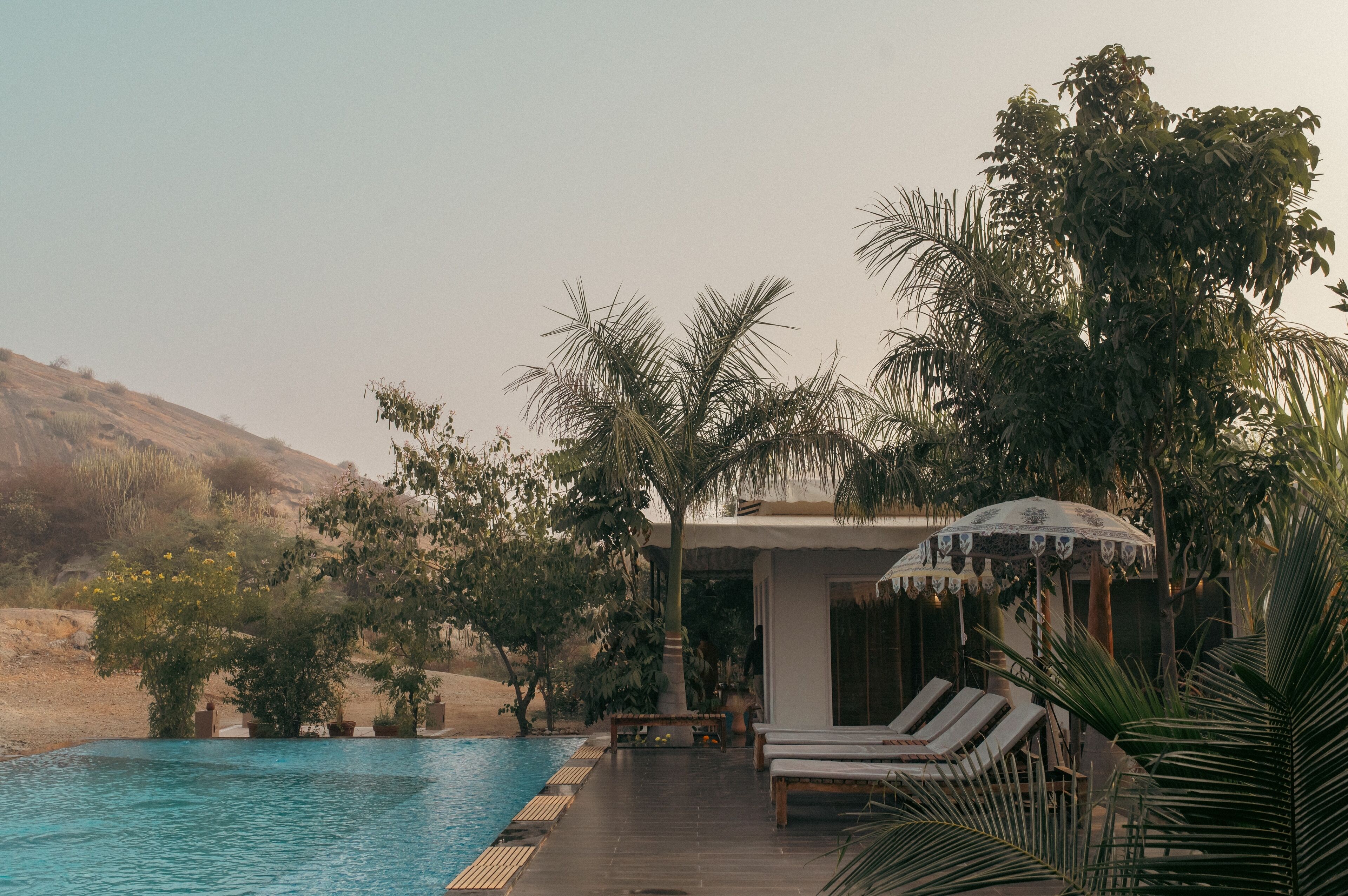 A poolside area with lounge chairs, a covered seating area, and a view of the surrounding landscape.