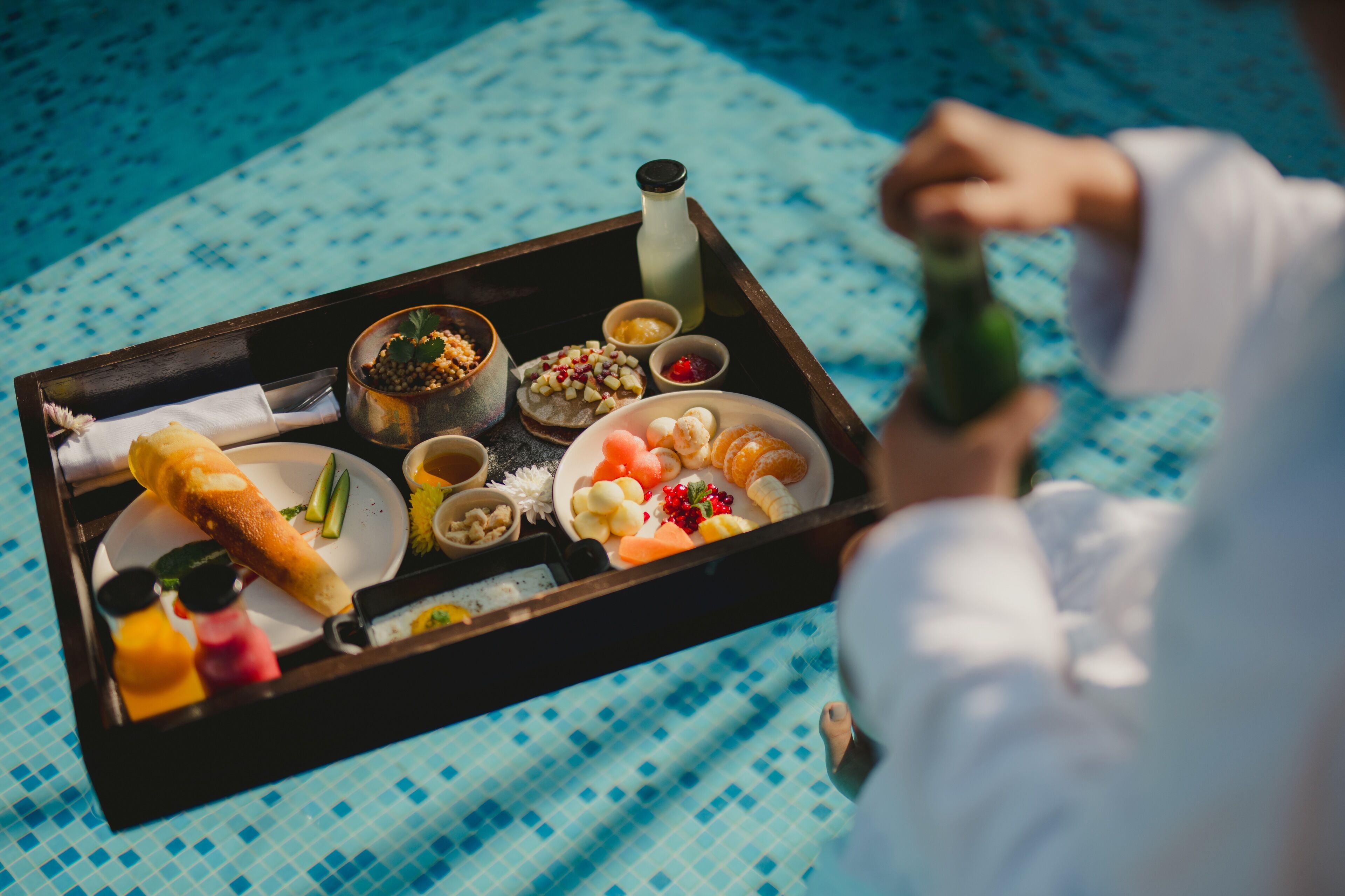 A tray with various food items including bread, fruits, and condiments, held by a person.