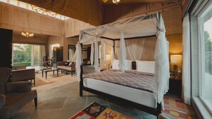 A spacious room with a four-poster bed, a sitting area with a sofa and chairs, and a large window providing a view of the outdoors. - Brij Pola, Jawai - Luxury Jungle Camp with Private Pools (Bali)