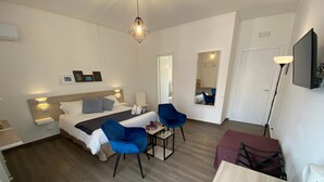 A hotel room with a bed, two blue chairs, a small table, a mirror, and a TV.