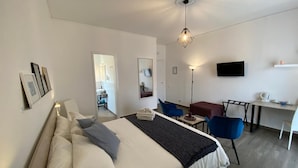 A hotel room with a bed, a desk, a chair, a TV, and a mirror.
