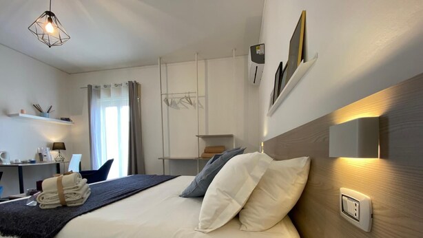 A modern hotel room with a neatly made bed, a desk with a lamp, and a view of the outdoors through large windows.