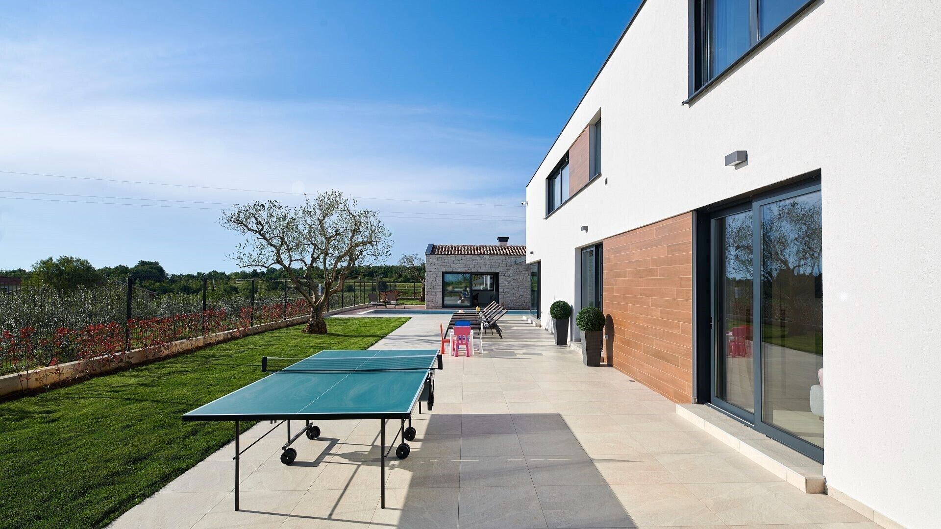 Un bâtiment moderne doté d’un patio comprenant une table de ping-pong, des sièges d’extérieur et un petit jardin.