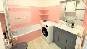 Un baño con bañera, lavadora y lavabo con espejo.