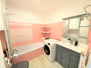 A bathroom with a bathtub, a washing machine, and a sink with a mirror above it. - Apartment for 2, 50m from Beaches, WIFI and Parking (Trégastel)